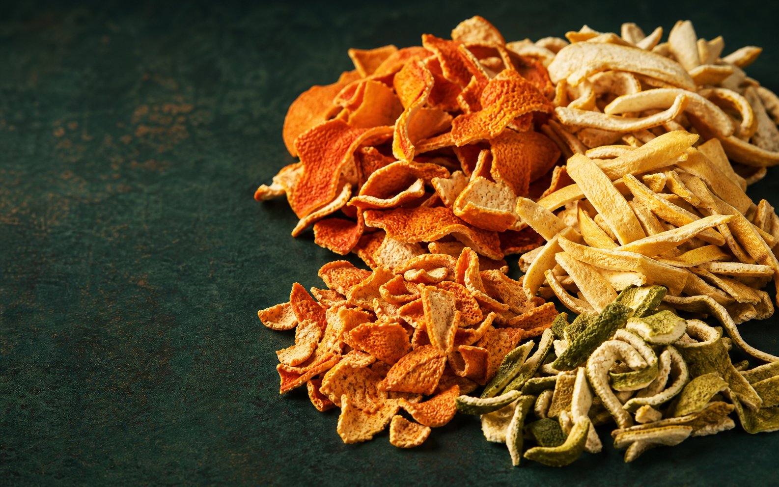 Dried orange, lemon, tangerine and lime peel arranged on a deep green surface